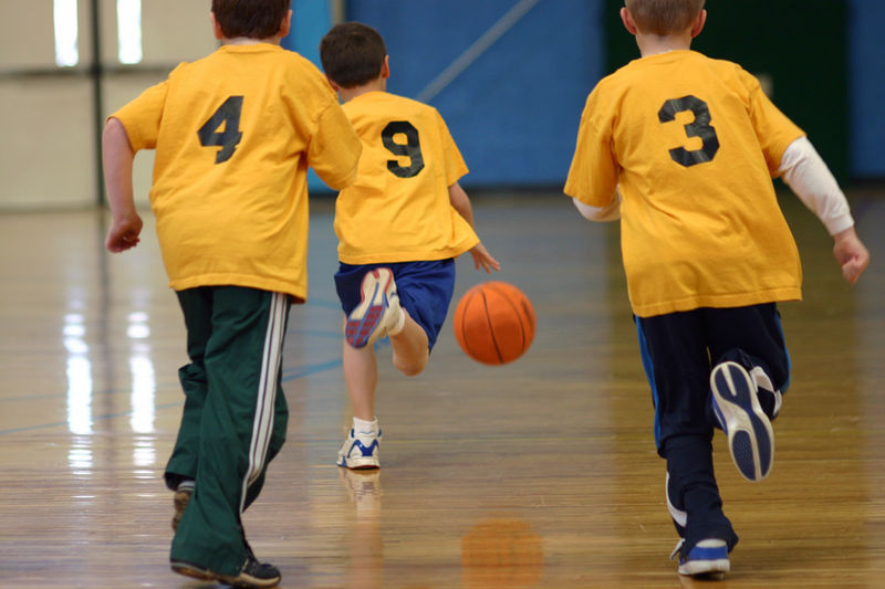 Children playing basketball in a gym, numbered shirts.